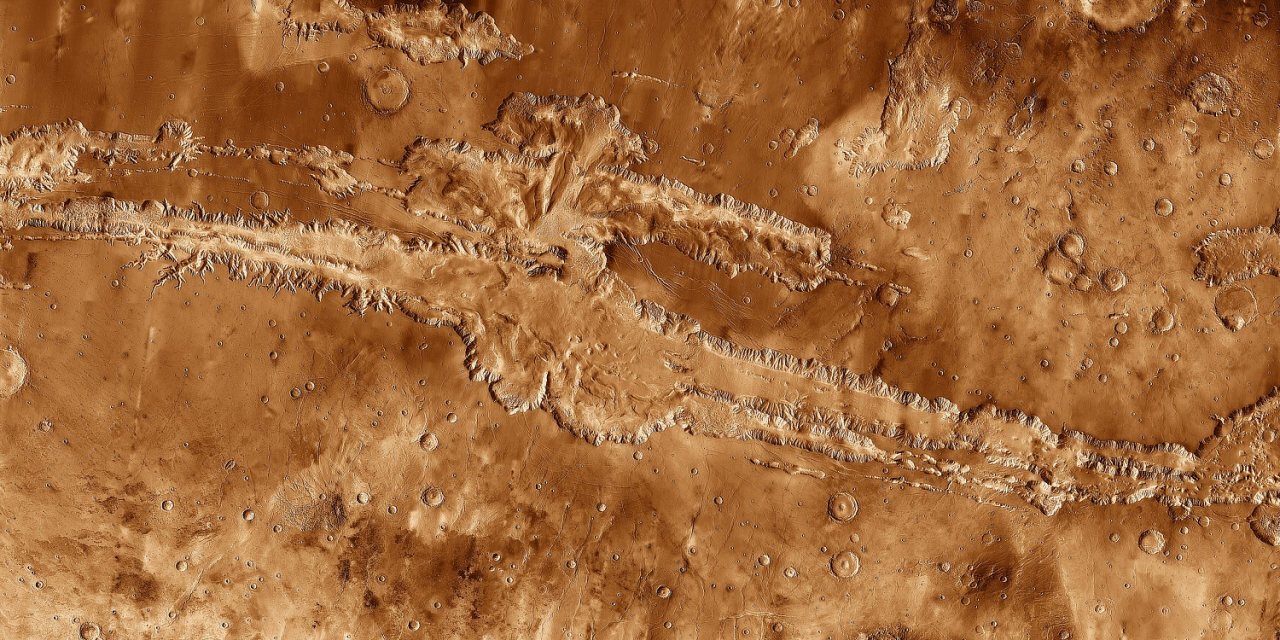 High-resolution orbital mosaic of Valles Marineris on Mars, showing an enormous canyon system stretching across the reddish Martian surface with branching chasms, cliffs, and impact craters.
