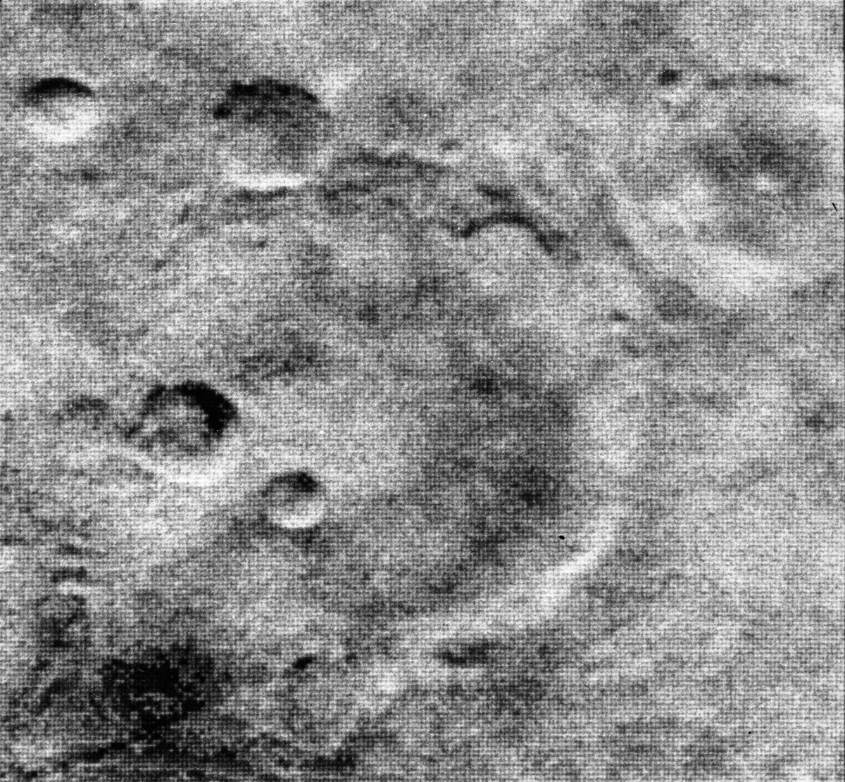 Black-and-white close-up image of the Martian surface taken by Mariner 4 in 1965, showing a rough, cratered landscape with no visible canal network.